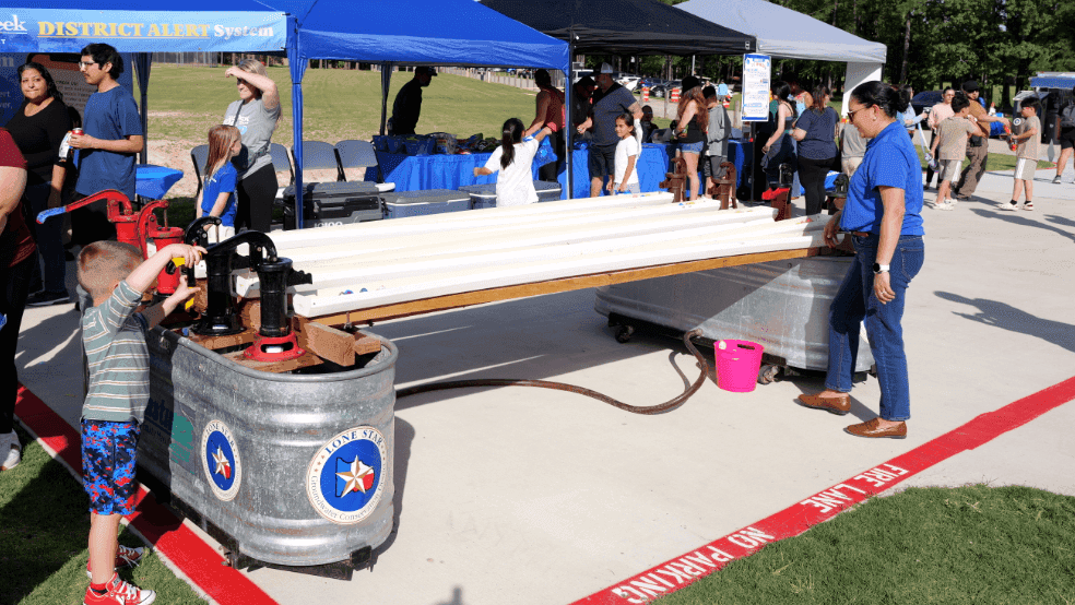 Attendees visit an educational mobile exhibit for the Lone Star Groundwater Conservation District, featuring informational displays under a blue awning.